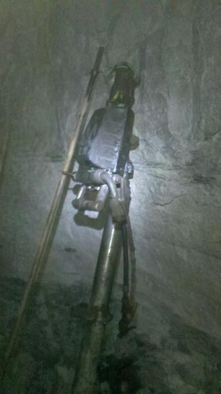 A jackleg drill leaning against the rock wall at the bottom of the shaft